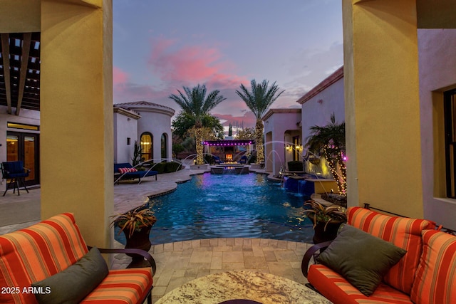 pool at dusk featuring a patio, an outdoor living space, pool water feature, and an in ground hot tub