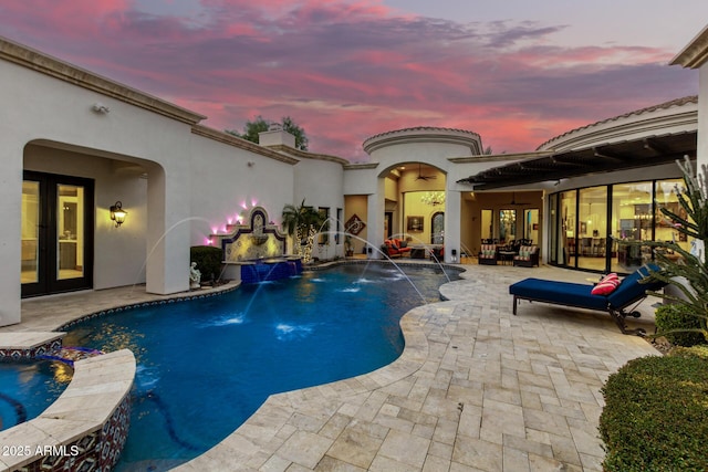 pool at dusk with a patio, pool water feature, ceiling fan, and french doors