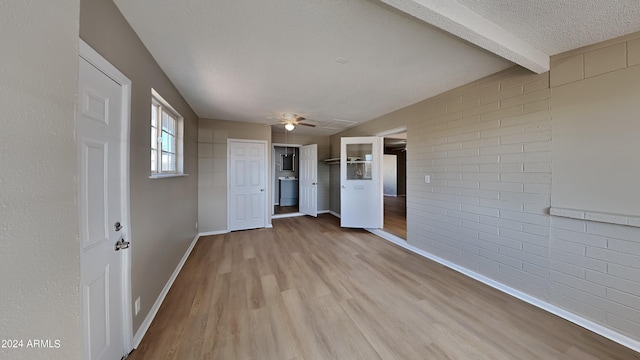 interior space featuring ceiling fan, a textured ceiling, beamed ceiling, light hardwood / wood-style floors, and brick wall