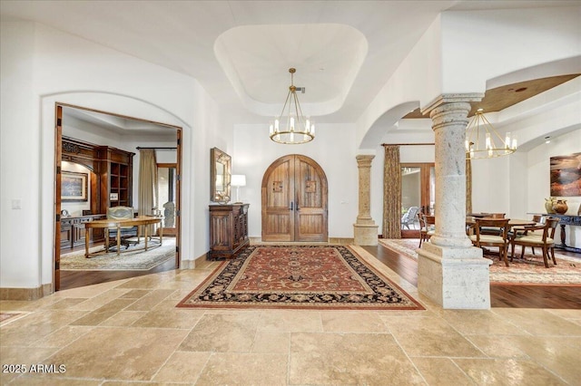 entryway featuring a notable chandelier, decorative columns, a raised ceiling, and a high ceiling