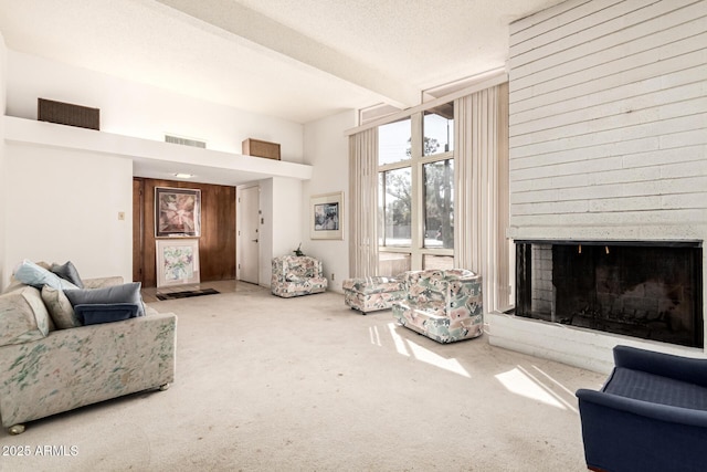 carpeted living room featuring a large fireplace, a textured ceiling, and beam ceiling