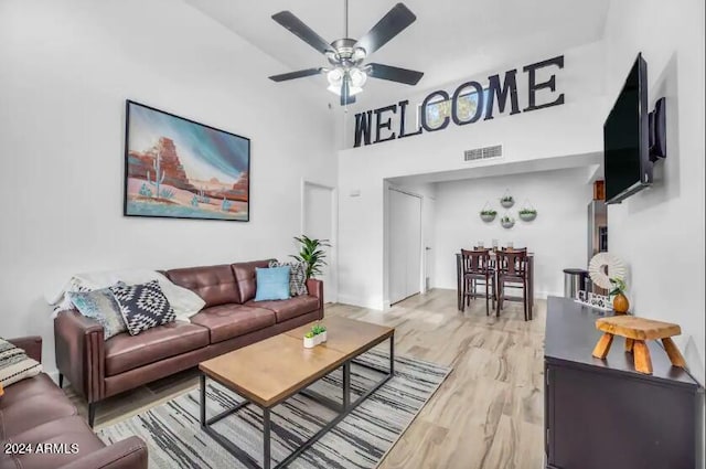 living room with a high ceiling, ceiling fan, and light wood-type flooring