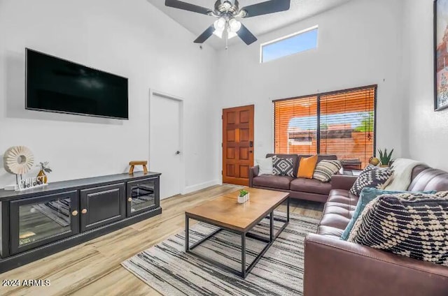 living room featuring ceiling fan, a towering ceiling, and light wood-type flooring