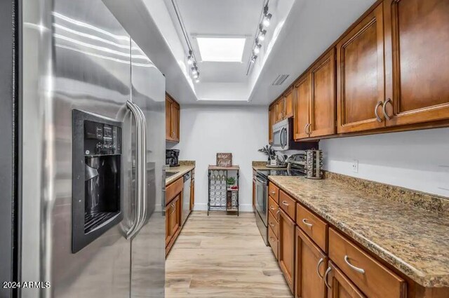 kitchen with appliances with stainless steel finishes, light hardwood / wood-style flooring, a skylight, a raised ceiling, and track lighting