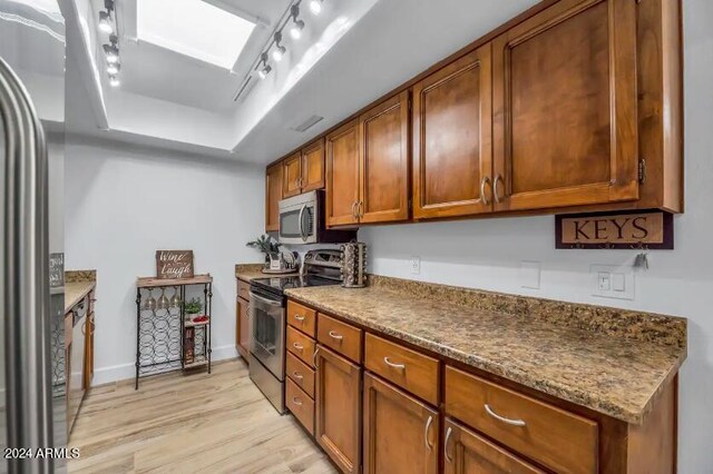 kitchen with light hardwood / wood-style flooring, a tray ceiling, track lighting, appliances with stainless steel finishes, and stone countertops