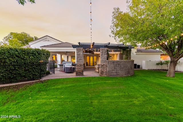 back house at dusk with a lawn, a patio area, and exterior kitchen