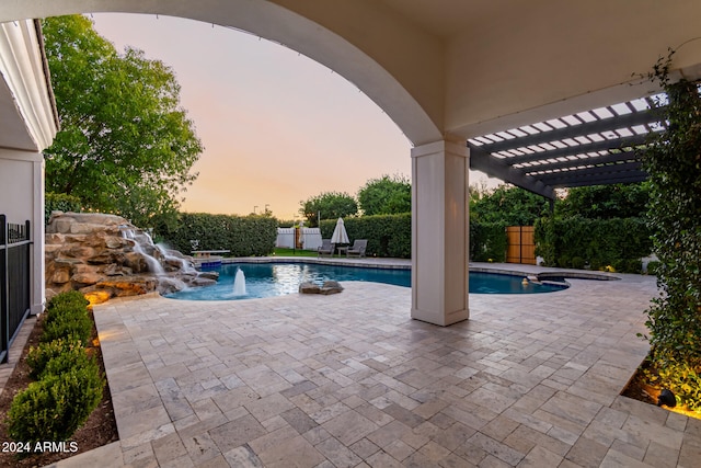 pool at dusk featuring a hot tub, pool water feature, and a patio