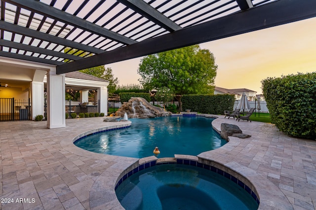 pool at dusk with a patio, pool water feature, and an in ground hot tub