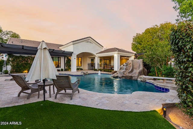 pool at dusk with pool water feature and a patio area