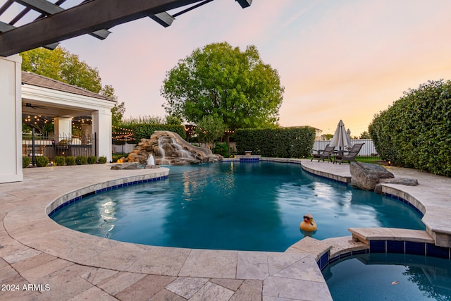 pool at dusk with an in ground hot tub, pool water feature, and a patio area