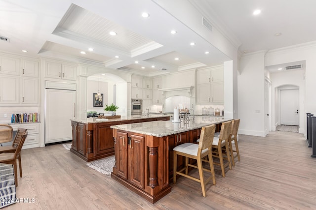 kitchen with light stone countertops, a kitchen bar, a spacious island, paneled built in refrigerator, and light wood-type flooring