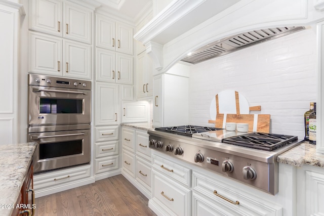 kitchen featuring light stone counters, hardwood / wood-style floors, custom range hood, white cabinetry, and appliances with stainless steel finishes