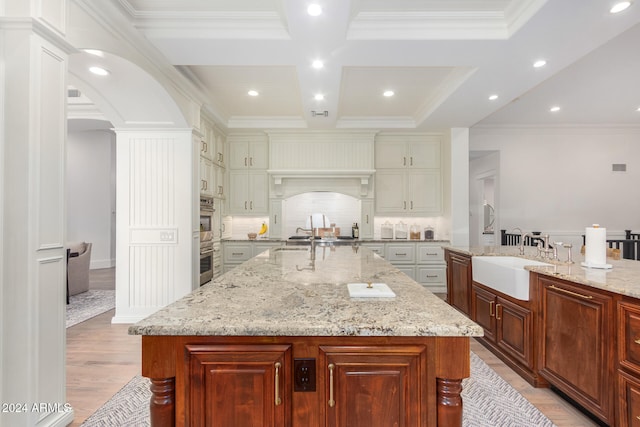 kitchen featuring light stone counters, crown molding, a spacious island, sink, and light hardwood / wood-style flooring