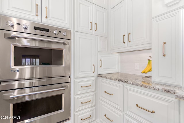 kitchen with tasteful backsplash, stainless steel double oven, light stone countertops, and white cabinets