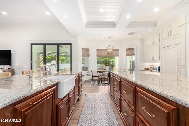 kitchen with wood-type flooring, light stone counters, hanging light fixtures, sink, and ornamental molding