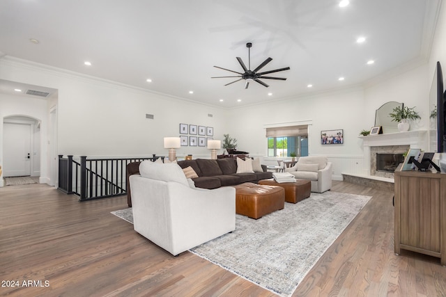 living room with dark wood-type flooring, a premium fireplace, ceiling fan, and ornamental molding