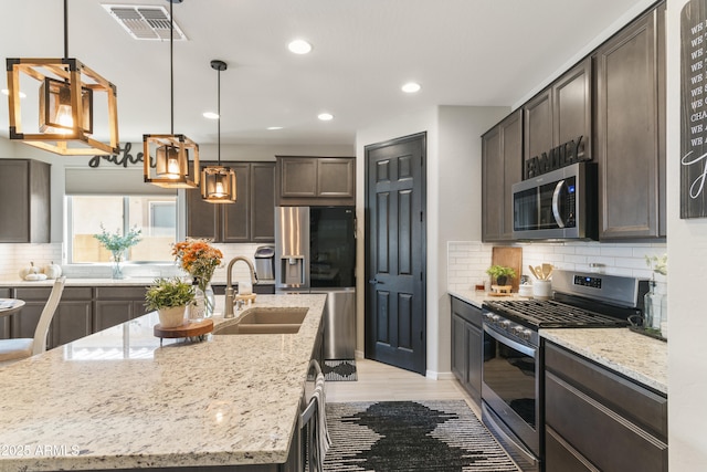 kitchen with light stone counters, dark brown cabinetry, stainless steel appliances, sink, and a center island with sink