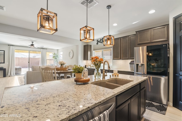 kitchen with light stone countertops, tasteful backsplash, dark brown cabinetry, sink, and stainless steel fridge with ice dispenser