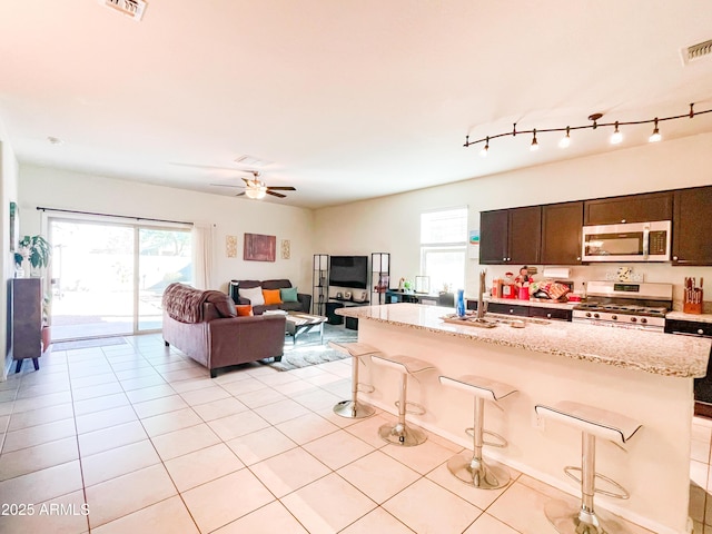 kitchen featuring stainless steel appliances, ceiling fan, a kitchen bar, dark brown cabinets, and light tile patterned flooring