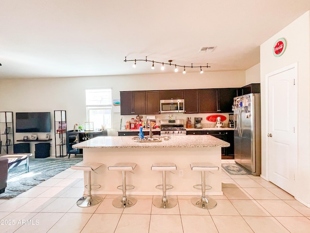 kitchen featuring a center island with sink, a breakfast bar area, appliances with stainless steel finishes, light tile patterned floors, and sink