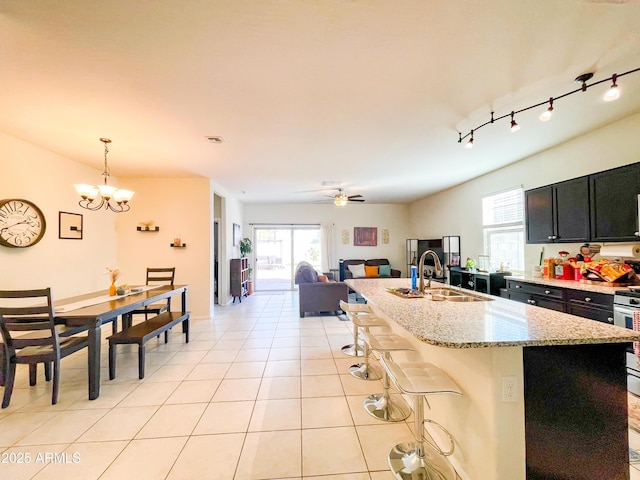 kitchen with sink, light tile patterned floors, an island with sink, ceiling fan with notable chandelier, and pendant lighting