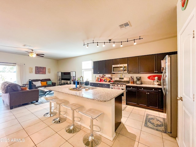 kitchen featuring stainless steel appliances, an island with sink, light tile patterned floors, a kitchen bar, and sink