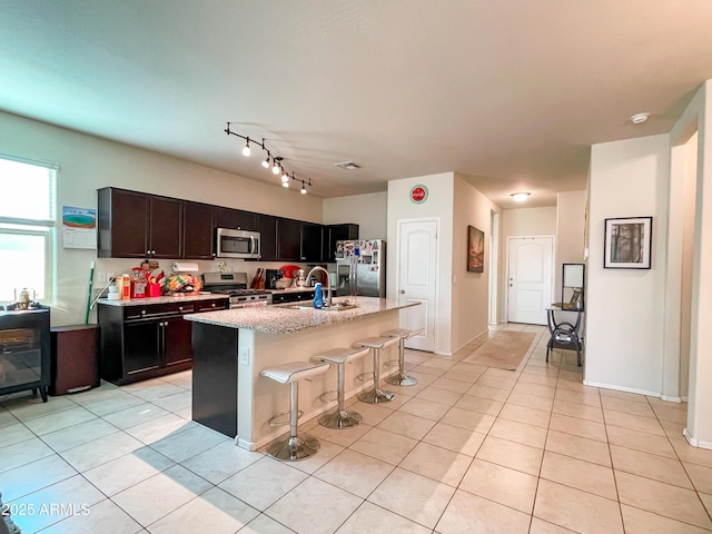 kitchen with a center island with sink, appliances with stainless steel finishes, light tile patterned floors, a breakfast bar, and sink