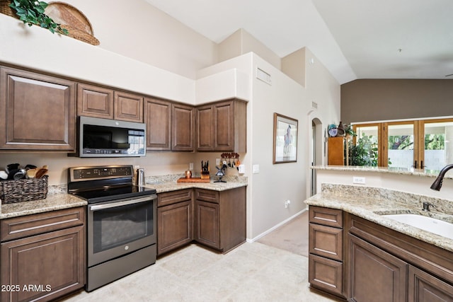 11861 E Becker Ln, Scottsdale, AZ 85259 - kitchen with stainless steel appliances, vaulted ceiling, light stone counters, light tile patterned floors, and dark brown cabinetry