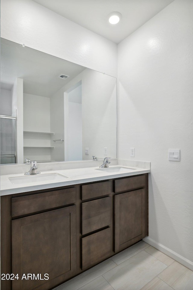 bathroom with baseboards, double vanity, a sink, and a shower stall