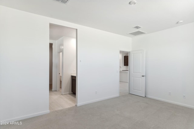 unfurnished bedroom featuring light carpet, visible vents, baseboards, and ensuite bathroom