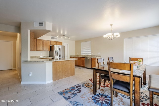 kitchen with kitchen peninsula, pendant lighting, light tile patterned floors, light stone countertops, and stainless steel appliances