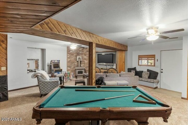 game room featuring ceiling fan, a wood stove, a textured ceiling, and carpet flooring