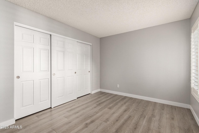 unfurnished bedroom featuring a textured ceiling, a closet, and light hardwood / wood-style floors