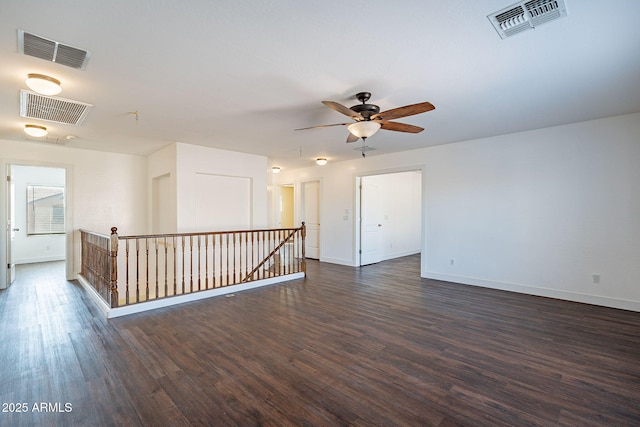 empty room featuring dark wood-style flooring, visible vents, and baseboards