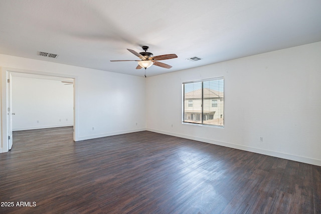 empty room with dark wood-style flooring, visible vents, and baseboards