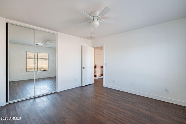 unfurnished bedroom with dark wood-style floors, a closet, visible vents, a ceiling fan, and baseboards