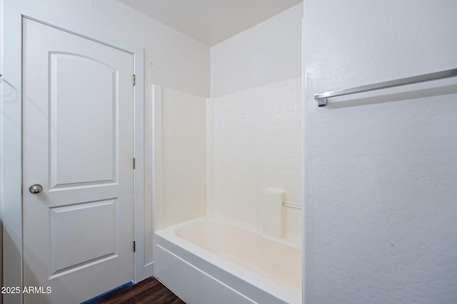 full bathroom with a textured wall, shower / bath combination, and wood finished floors