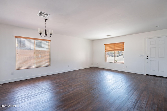 empty room featuring a chandelier, visible vents, baseboards, and dark wood-style floors