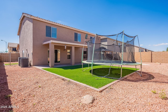 rear view of house with a patio, a fenced backyard, a trampoline, central air condition unit, and stucco siding