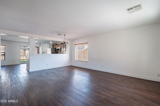 unfurnished living room featuring a notable chandelier, dark wood finished floors, visible vents, and baseboards