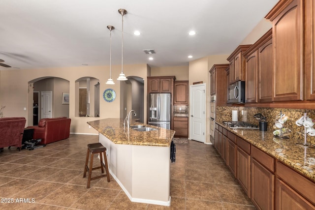 kitchen featuring stainless steel appliances, sink, pendant lighting, decorative backsplash, and a kitchen island with sink