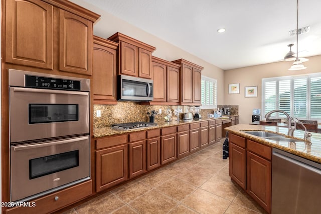 kitchen featuring stainless steel appliances, sink, tasteful backsplash, light stone countertops, and pendant lighting