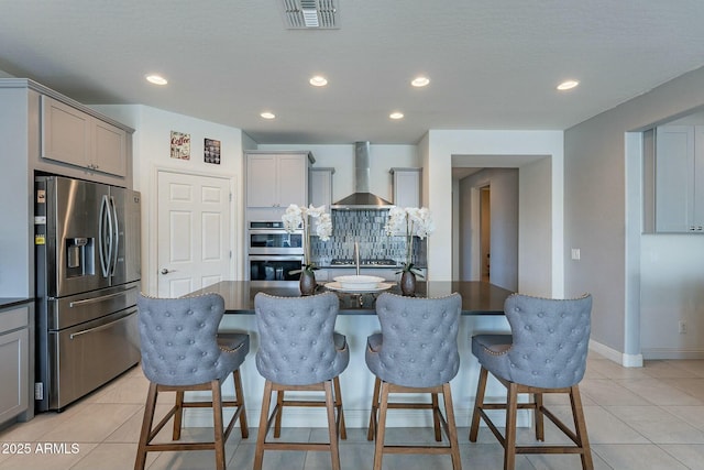 kitchen featuring stainless steel appliances, gray cabinets, a center island with sink, and wall chimney range hood