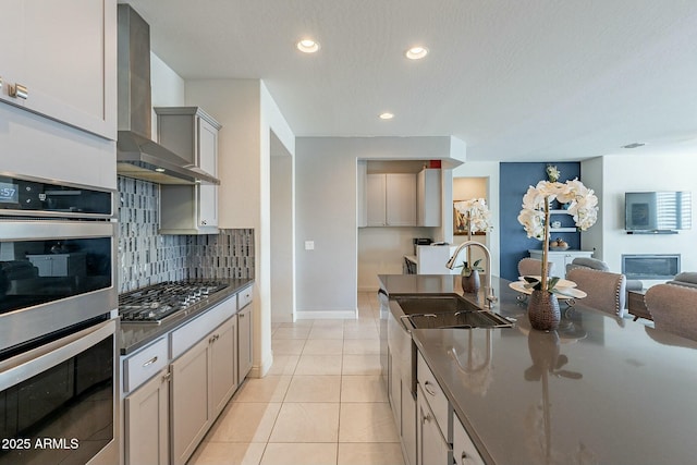 kitchen with light tile patterned floors, sink, appliances with stainless steel finishes, tasteful backsplash, and wall chimney exhaust hood