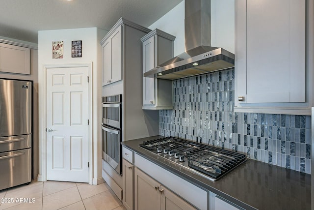 kitchen featuring light tile patterned floors, appliances with stainless steel finishes, gray cabinets, decorative backsplash, and wall chimney range hood