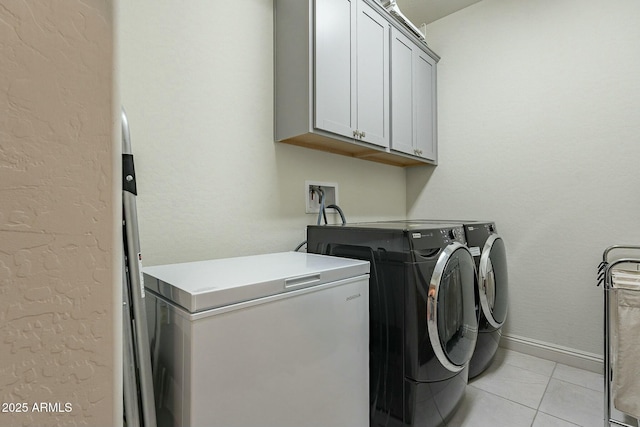 clothes washing area featuring separate washer and dryer, light tile patterned floors, and cabinets