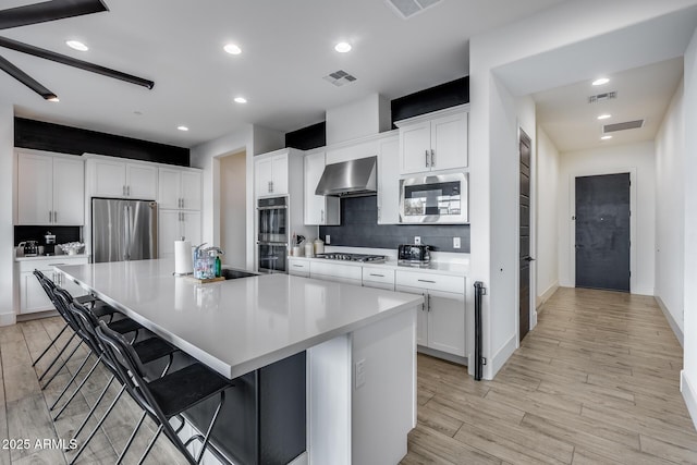 kitchen featuring stainless steel appliances, white cabinetry, wall chimney exhaust hood, and a spacious island