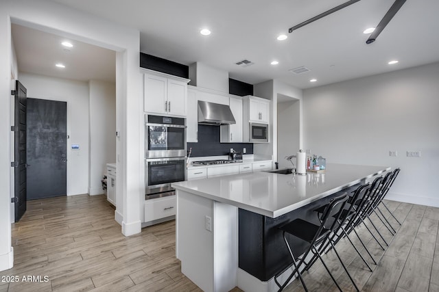 kitchen with white cabinets, a kitchen breakfast bar, sink, wall chimney exhaust hood, and stainless steel appliances