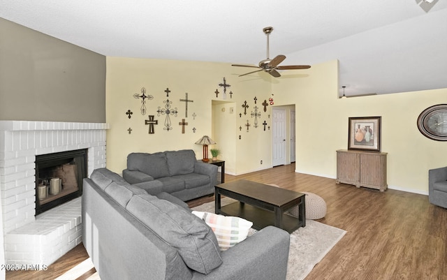 living room with hardwood / wood-style flooring, vaulted ceiling, ceiling fan, and a fireplace