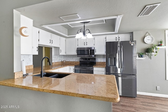 kitchen with sink, stainless steel appliances, kitchen peninsula, decorative light fixtures, and a raised ceiling